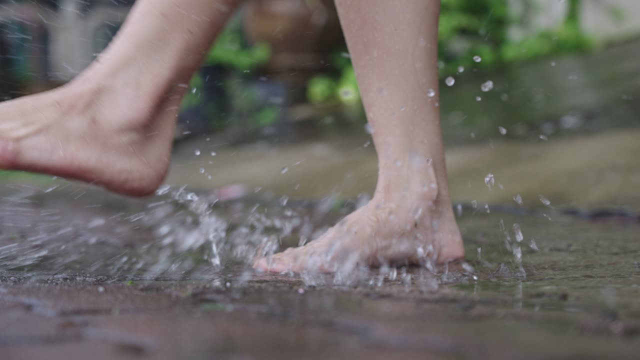 After raining activity, close up barefoot slowly stomping in water puddles on a paving cement footpath, tropical rainy season, climate changes, environmental issue, adult having fun with playing water