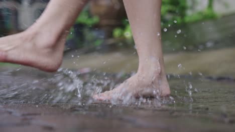 after raining activity, close up barefoot slowly stomping in water puddles on a paving cement footpath, tropical rainy season, climate changes, environmental issue, adult having fun with playing water