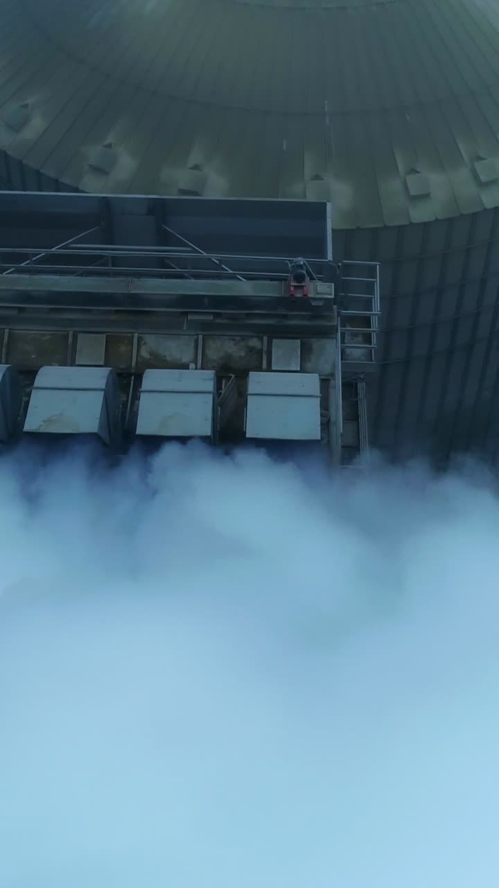 Five connected pipes producing heavy thick white smoke. Granary complex premises and tanks from aerial perspective on grey winter day. Vertical video