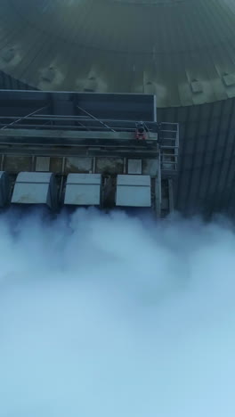 five connected pipes producing heavy thick white smoke. granary complex premises and tanks from aerial perspective on grey winter day. vertical video