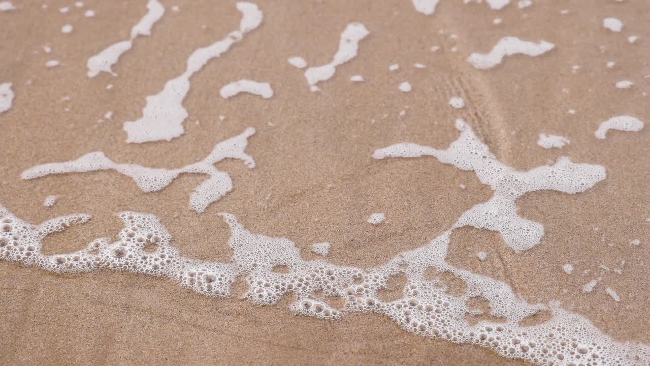 Waves retreat, leaving bubbles on sandy shore