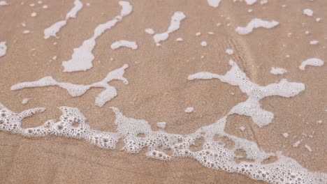 waves retreat, leaving bubbles on sandy shore