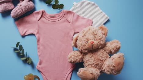 video of pink baby grow, booties, teddy bear and hat with copy space on blue background