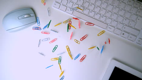 colourful paperclips falling in the middle of a white office desk