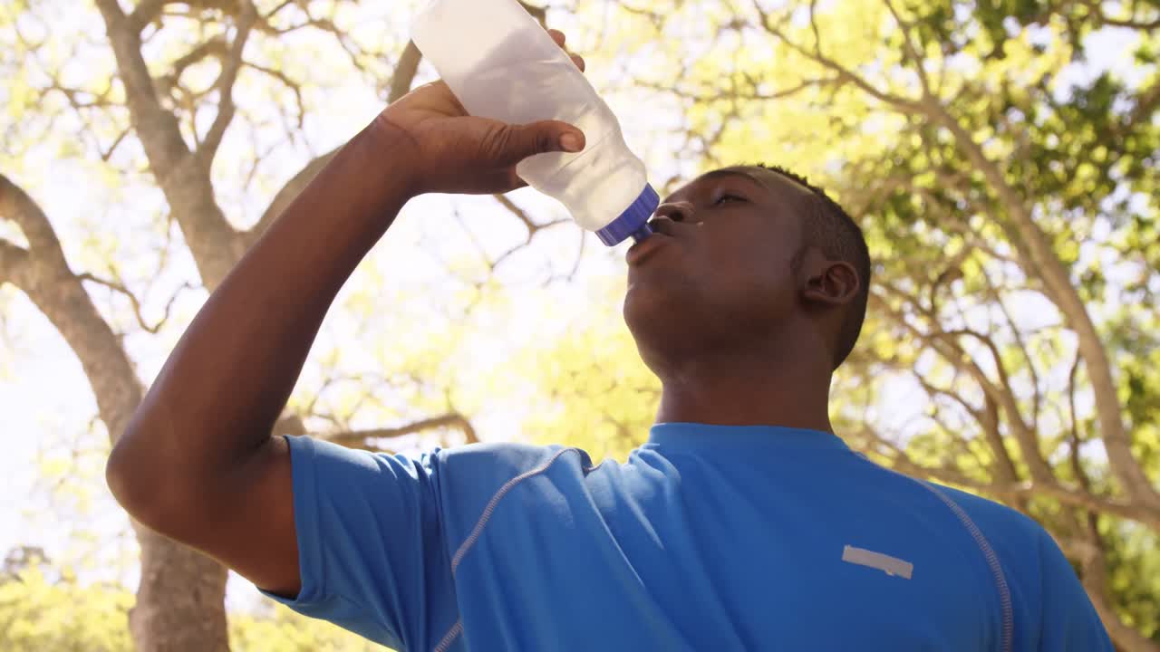 Contre-plongée d'un sportif qui boit à une gourde