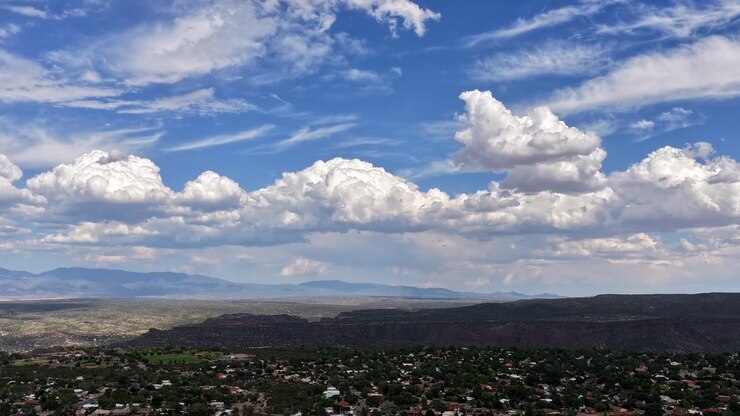 Timelapse panorámico de dron 4K UHD que captura rápidas nubes blancas barriendo un escarpado paisaje de cañón residencial. Casas suburbanas bordean las crestas de la topografía árida del valle occidental.