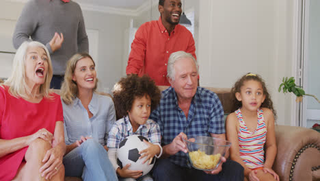 Video-Einer-Gemischten-Familie,-Die-Auf-Der-Couch-Sitzt-Und-Ein-Fußballspiel-Verfolgt