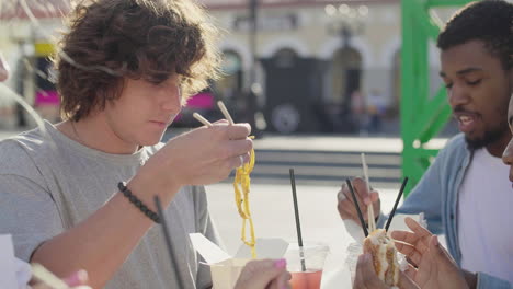 Grupo-De-Amigos-Comiendo-Comida-Callejera,-Sentados-En-Una-Mesa-Al-Aire-Libre-Mientras-Se-Divierten-Juntos