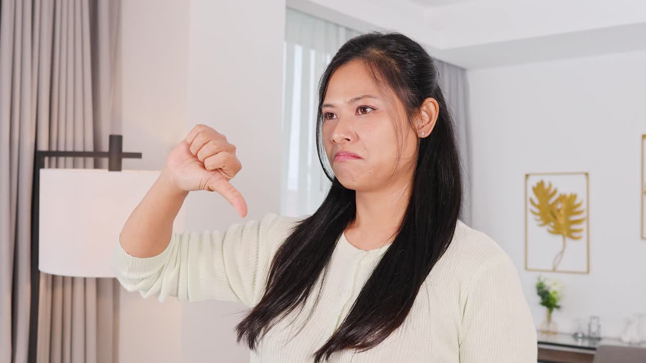 A woman shows thumbs up and down gestures in a well-lit living room, conveying approval and disapproval