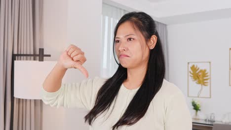 a woman shows thumbs up and down gestures in a well-lit living room, conveying approval and disapproval