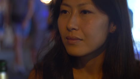 an asian woman in a busy asian horeca street contemplating with a bottle in front of her and nightlife passengers on the background