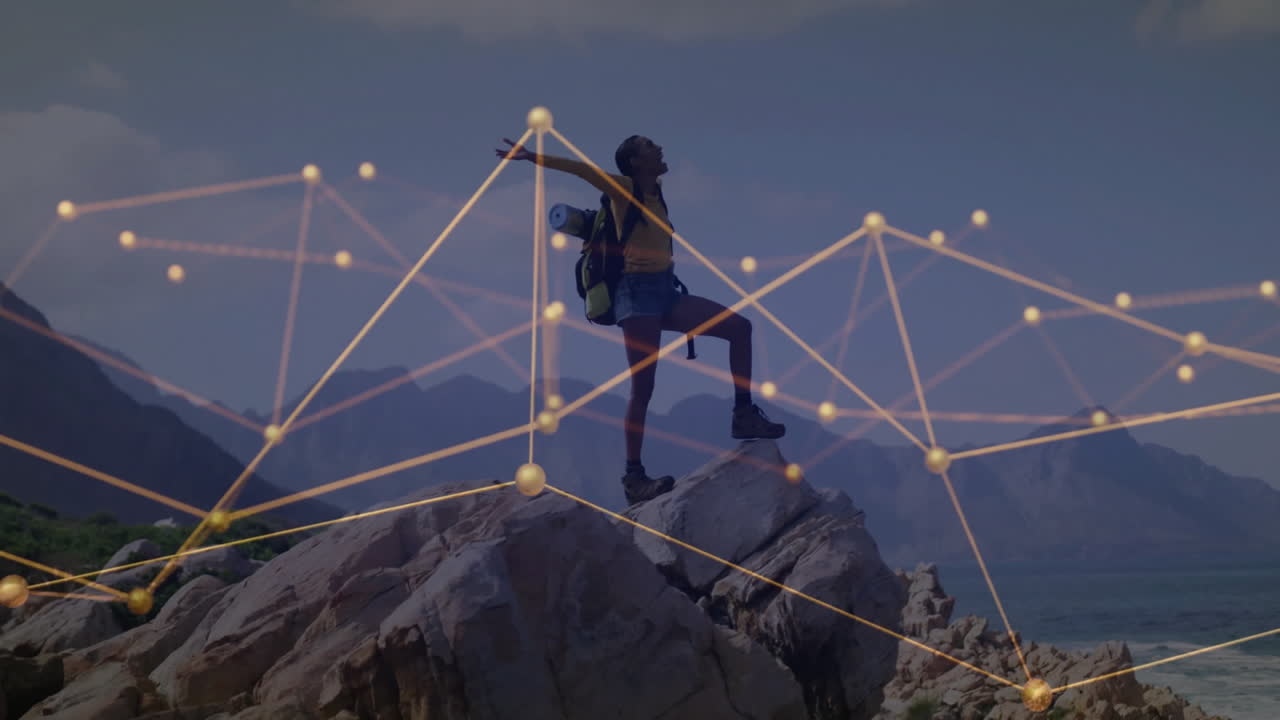 Woman hiker standing on rocky coast, celebrating technology, showing golden network nodes and lines