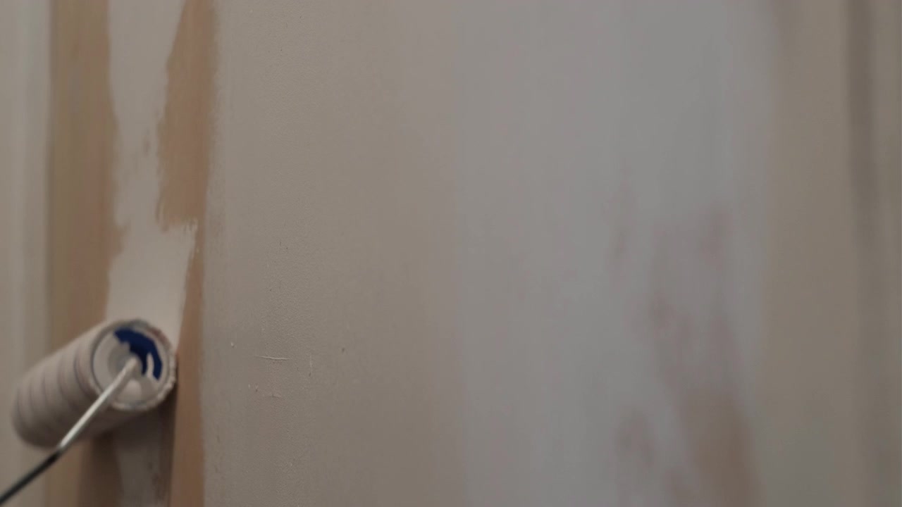 Close-up static shot of a roller applying white paint onto an interior wall during home renovation work