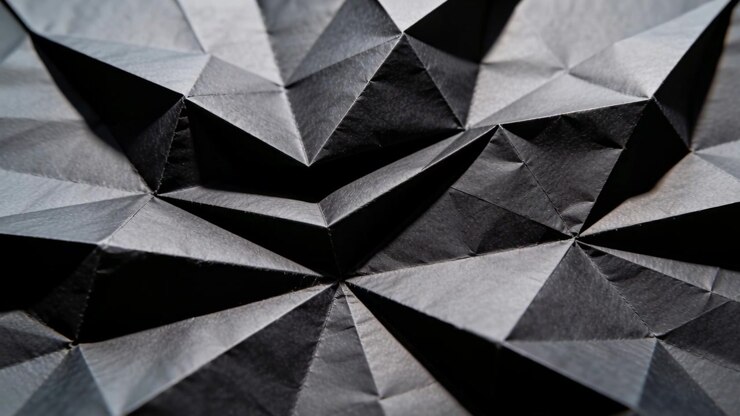 Moving camera showing dark folded paper at tabletop, revealing right facets to emphasize geometry