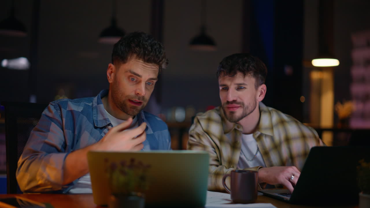 Two creators communicating night workplace interior. Young team brainstorming