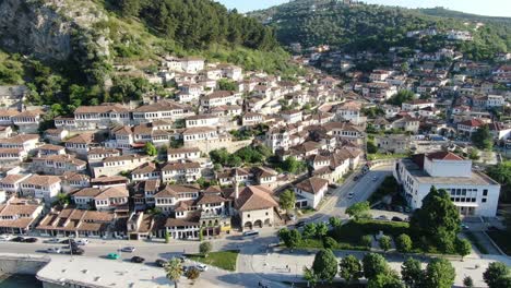 drone view in albania flying in berat town showing medieval houses with brick roofs next to a green mountain