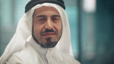 portrait of successful arab businessman in traditional outfit gently smiling, wearing white kandura and black agal keeping a ghutra in place. saudi, emirati, arab businessman concept.