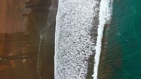 drone view of beautiful brown sandy beach with white waves washing on shore and turquoise blue water