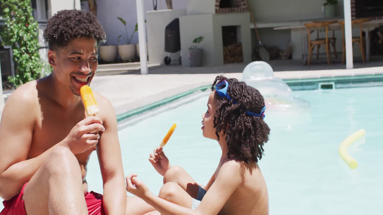 feliz hombre biracial y su hijo comiendo helado por la piscina en el jardín