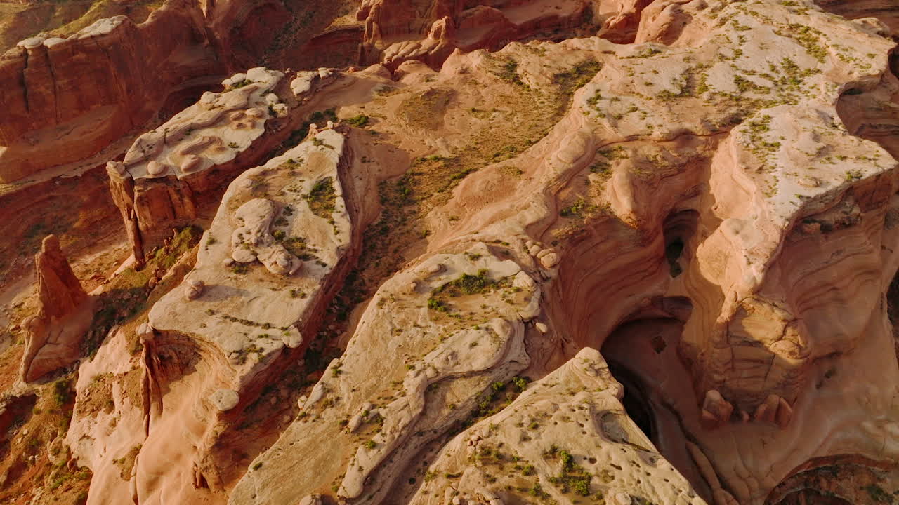 Unusual oddly-shaped red rocks of American canyons in Utah. Descending over a big rock with tiny greenery on top.