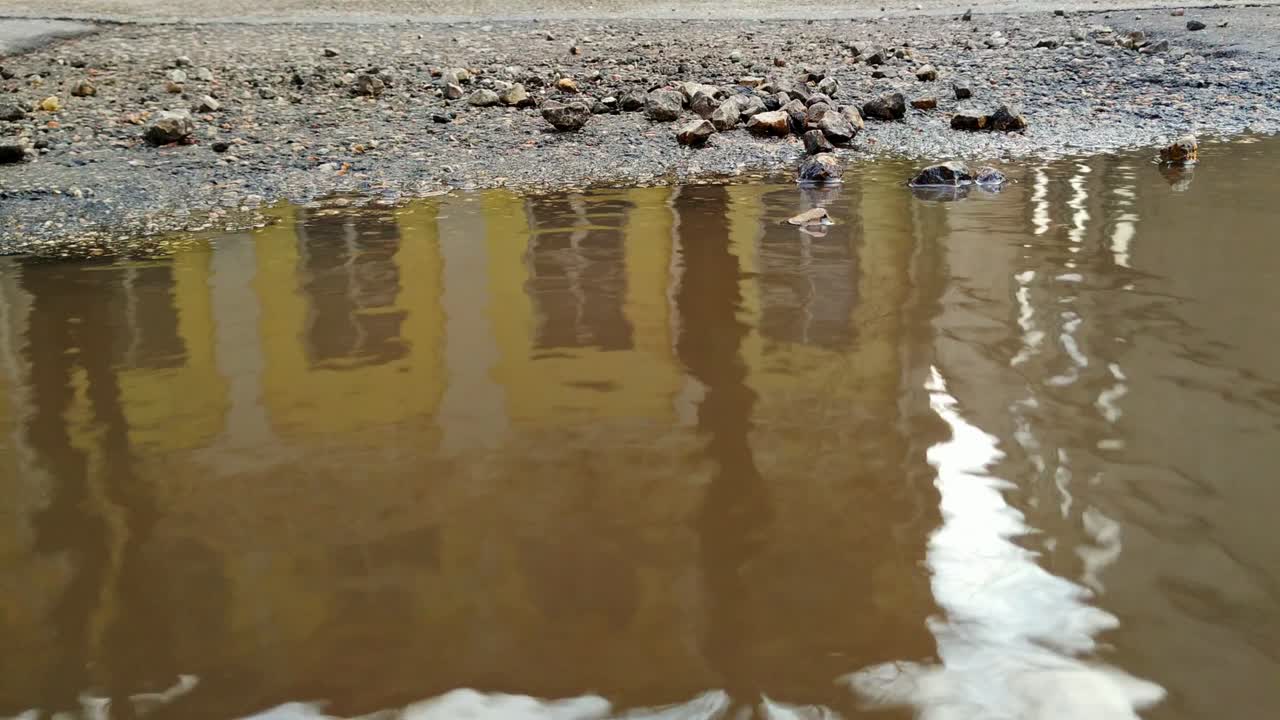 Murky brown street puddle, water ripples, closeup static high angle view, day