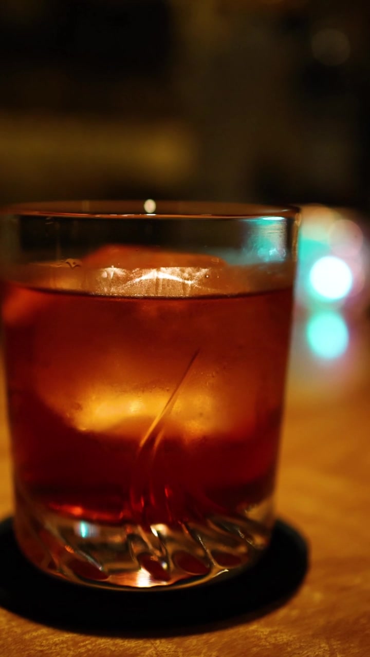 Un primo piano verticale di una bevanda ambrata ghiacciata su un bancone da bar con effetto bokeh