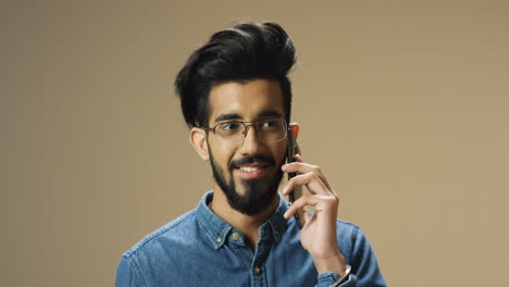 young handsome indian man with beard and glasses talking cheerfully on mobile phone and smiling