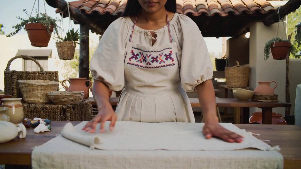 Donna in camicetta che stende un panno avorio e liscia le pieghe su un tavolo da patio, rivelando un tessuto sfrangiato