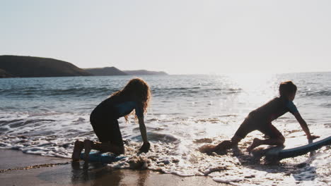 two silhouetted  children wearing wetsuits playing in sea with bodyboards on  summer beach vacation