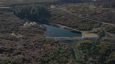 Vista-Aérea-De-Un-Pequeño-Depósito-De-Agua-Que-Recoge-La-Lluvia-Y-La-Dirige-Al-Depósito-De-Agua-Más-Grande-Al-Final-Del-Valle.