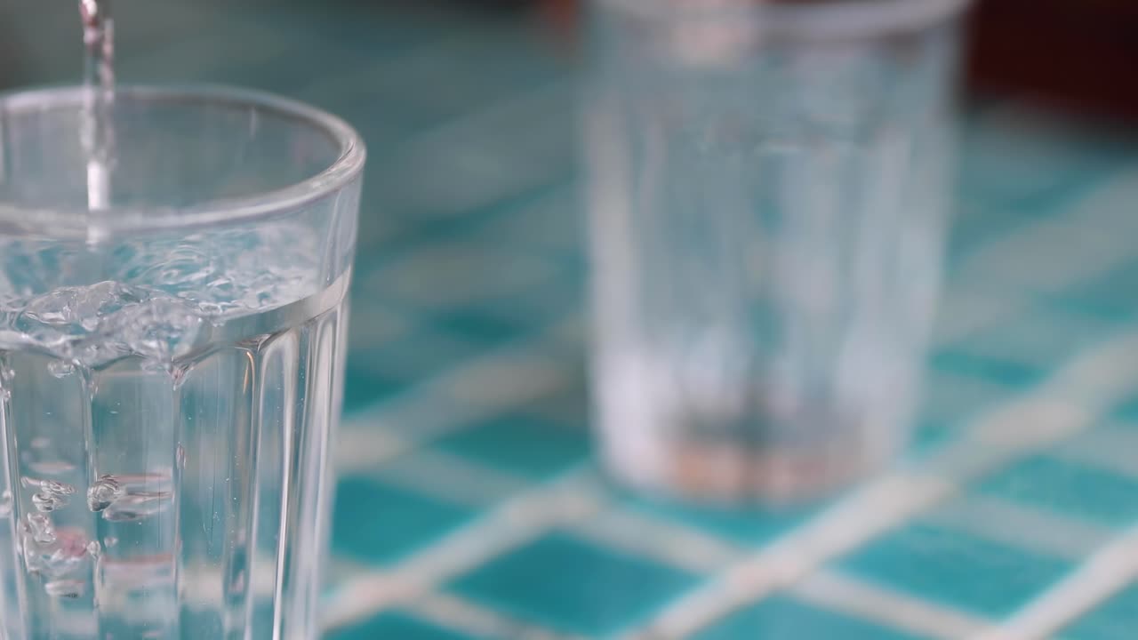 A detailed view of liquid being poured into a clear glass on a tiled surface.