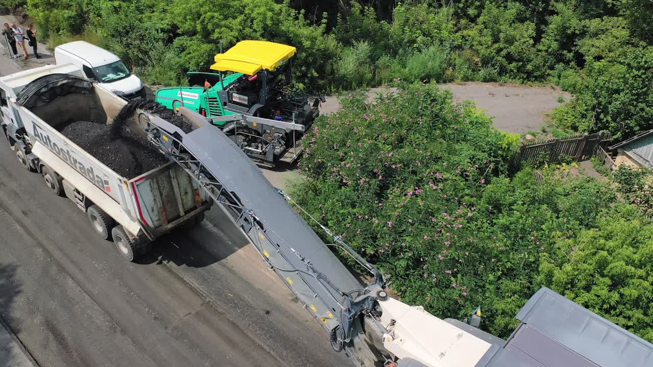 Construction of the new asphalt road. Special equipment replacing asphalt into the trailer on the road in summer. Top view.