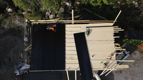 aerial view of a construction worker roofing a cabin among trees in daylight