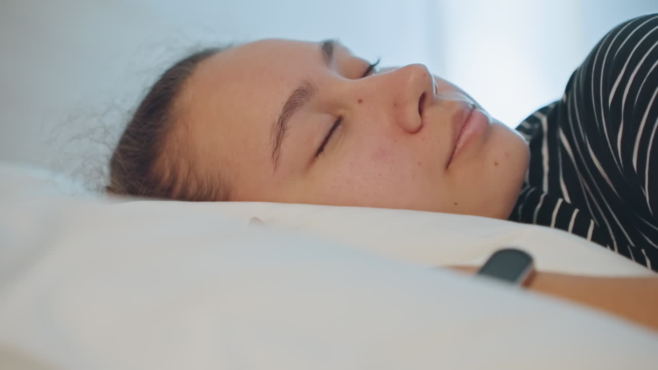 Hviler efter rejsen. Kvinde slapper af i fredfyldte hotelomgivelser. Træt kvindelig gæst slapper af i et dæmpet oplyst hotelrum. Asiatisk kvinde tager en afslappende pause på hyggelig hotelseng efter en travl dag.