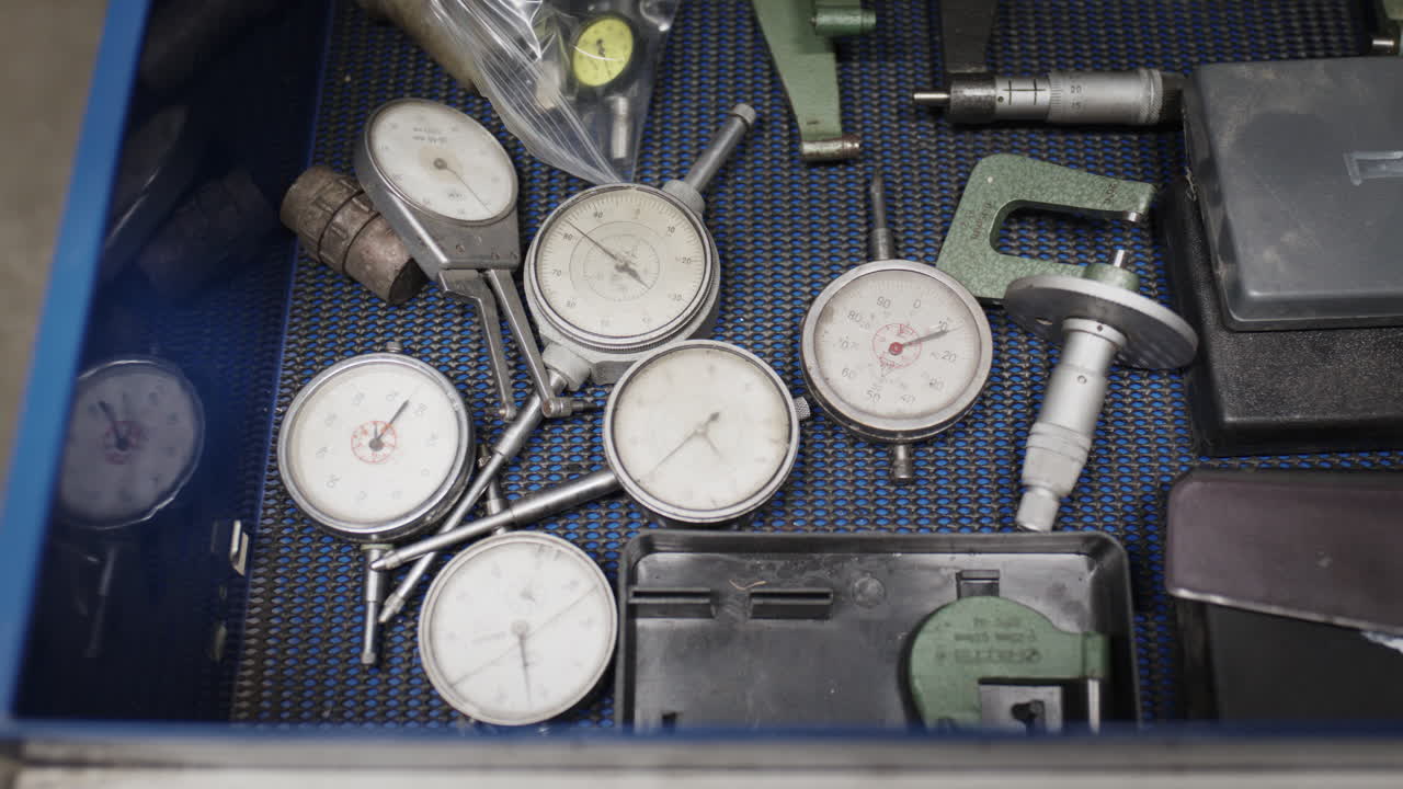 Vista dall'alto di un cassetto portautensili industriale che contiene indicatori a quadrante analogici, micrometri e calibri di precisione
