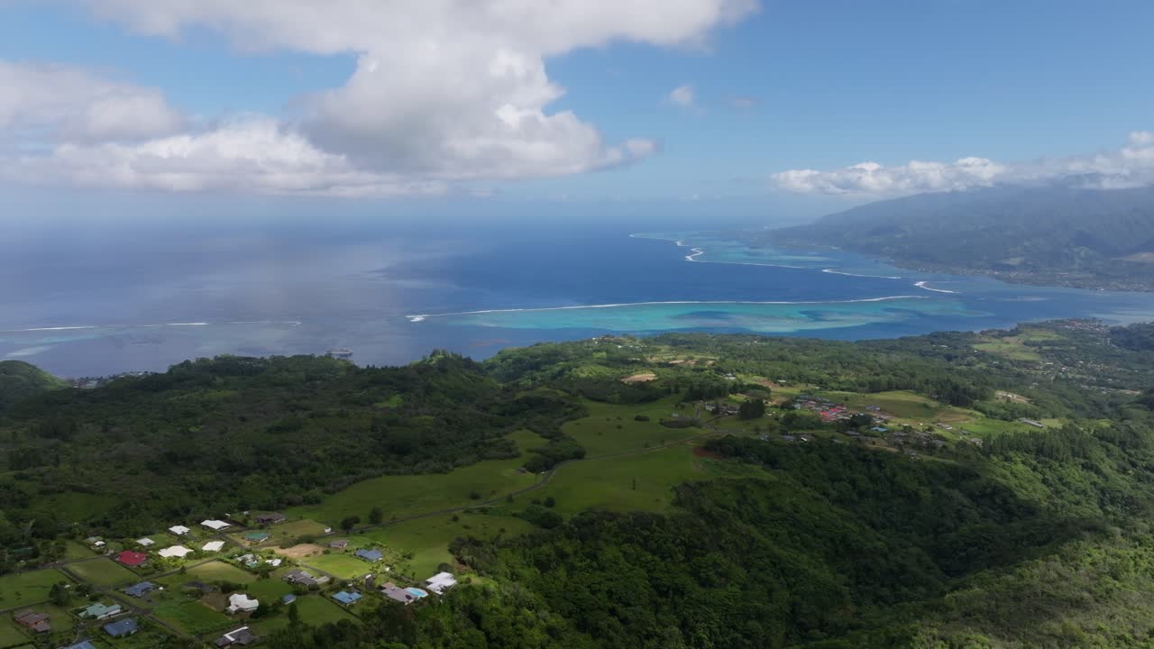 Drone views of the Tahitian coast with the blue waters and coral reefs in the background and lush greenery in the foreground on a partly cloudy day