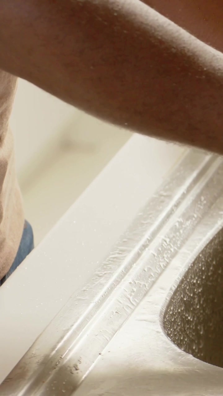 Vertical video: Entering man rinsing arm and torso at steel sink for cleaning, showing blue band