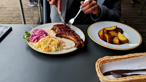 restaurant meal with grilled ribs, potato wedges, and coleslaw on outdoor table