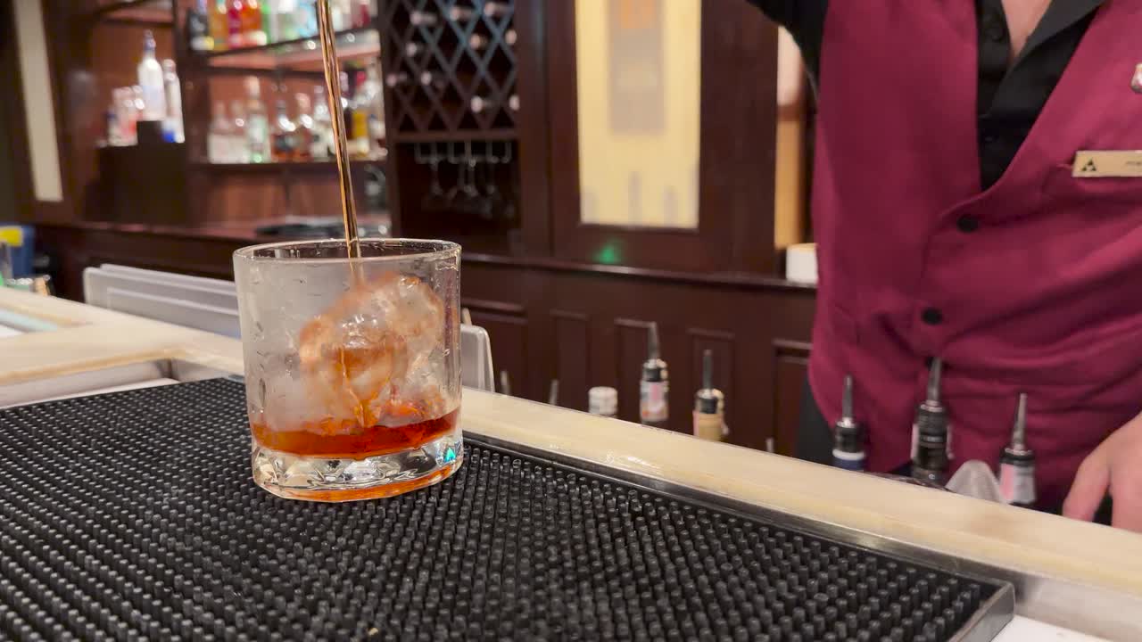Bartender pours and stirs Negroni cocktail in glass with ice at elegant hotel bar