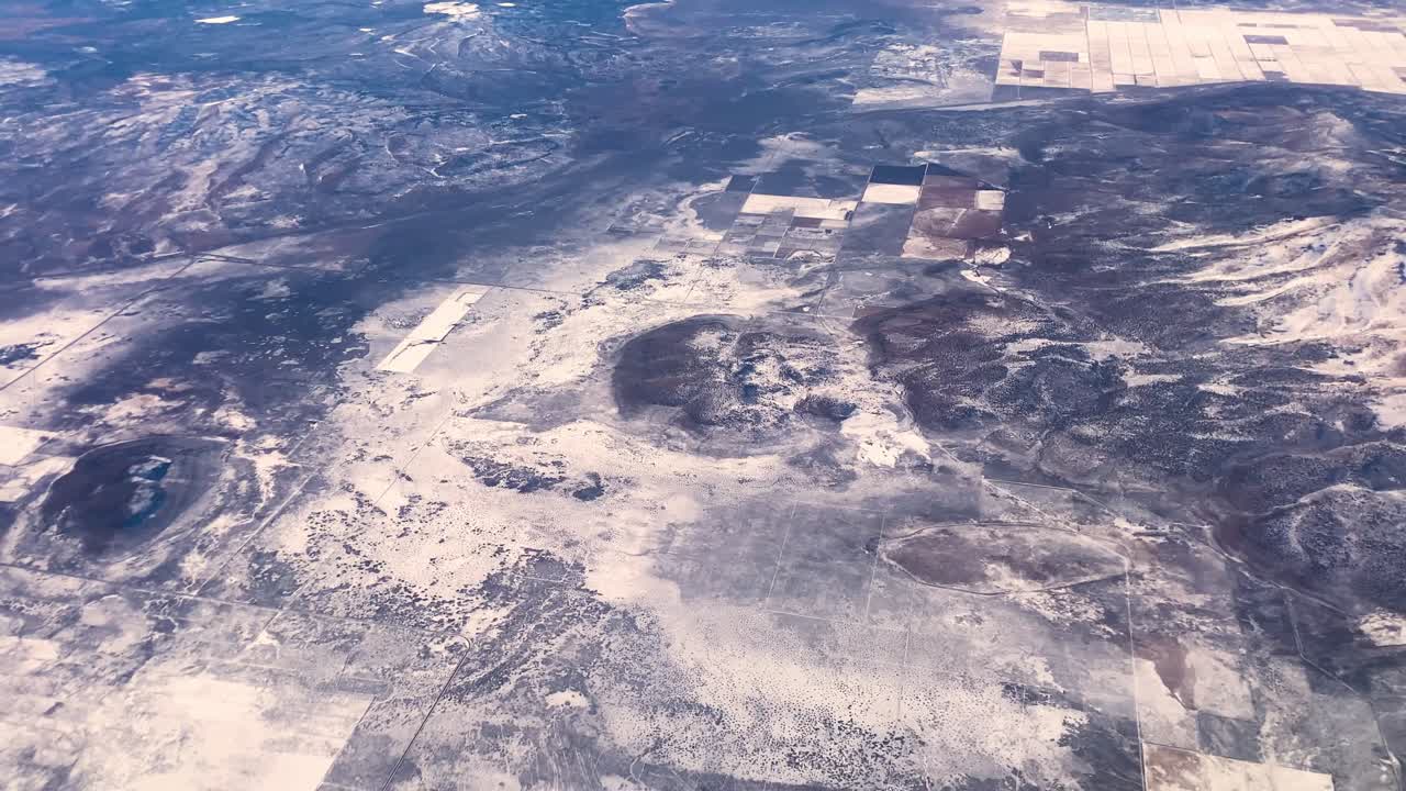 Dramatic aerial footage of landscape from airplane on a sunny day with snowy farmland and desert