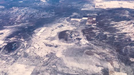 dramatic aerial footage of landscape from airplane on a sunny day with snowy farmland and desert