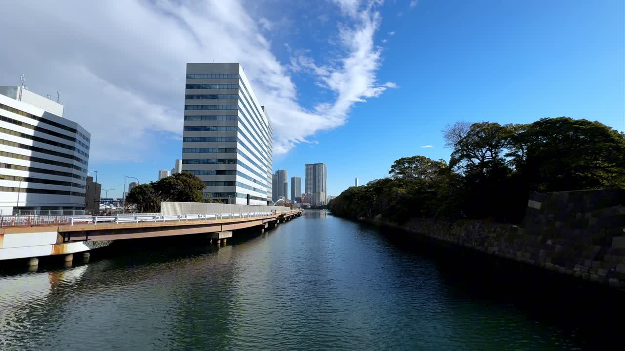 A serene canal view in Hama Rikyu Gardens with buildings, blue skies, and greenery