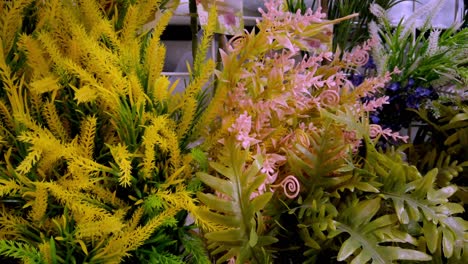 pan right of yellow and pink artificial flowers arranged with lush green foliage in display