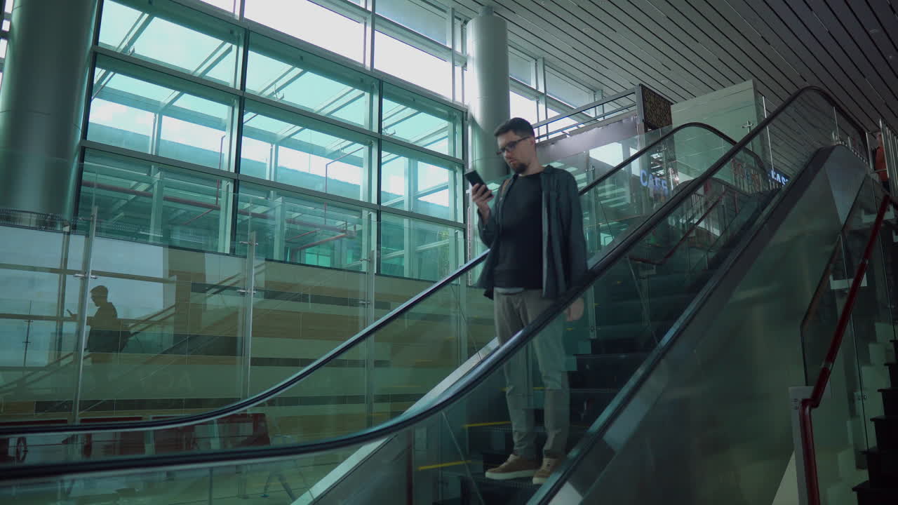 hombre usando un teléfono inteligente en la escalera mecánica del aeropuerto