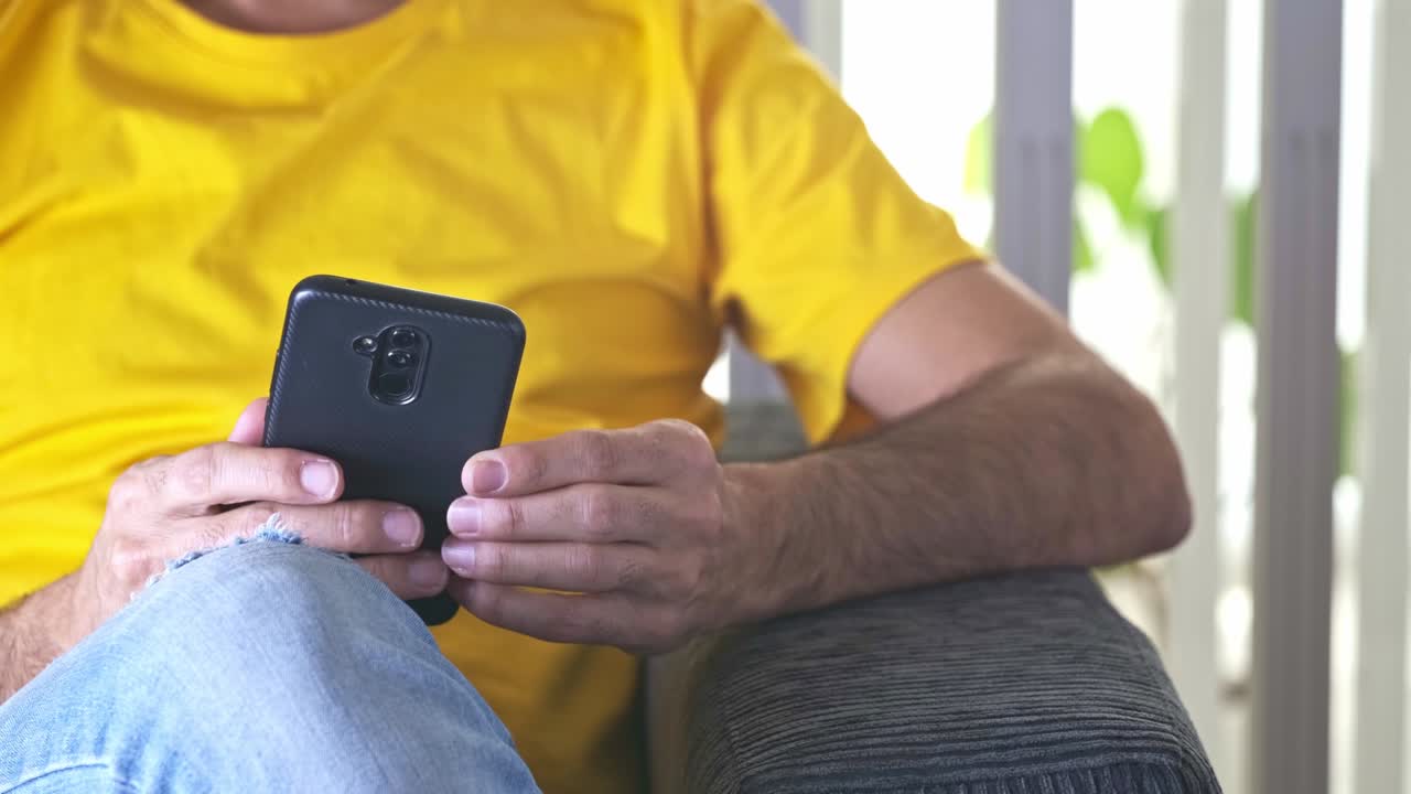 hombre de pelo oscuro sentado en un sofá con su teléfono inteligente en sus manos