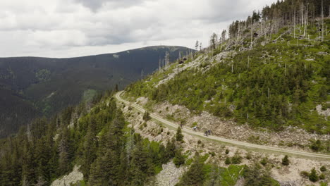 Cyclists-riding-bikes-on-trip-in-moravian-mountains,-Czechia,-drone-shot