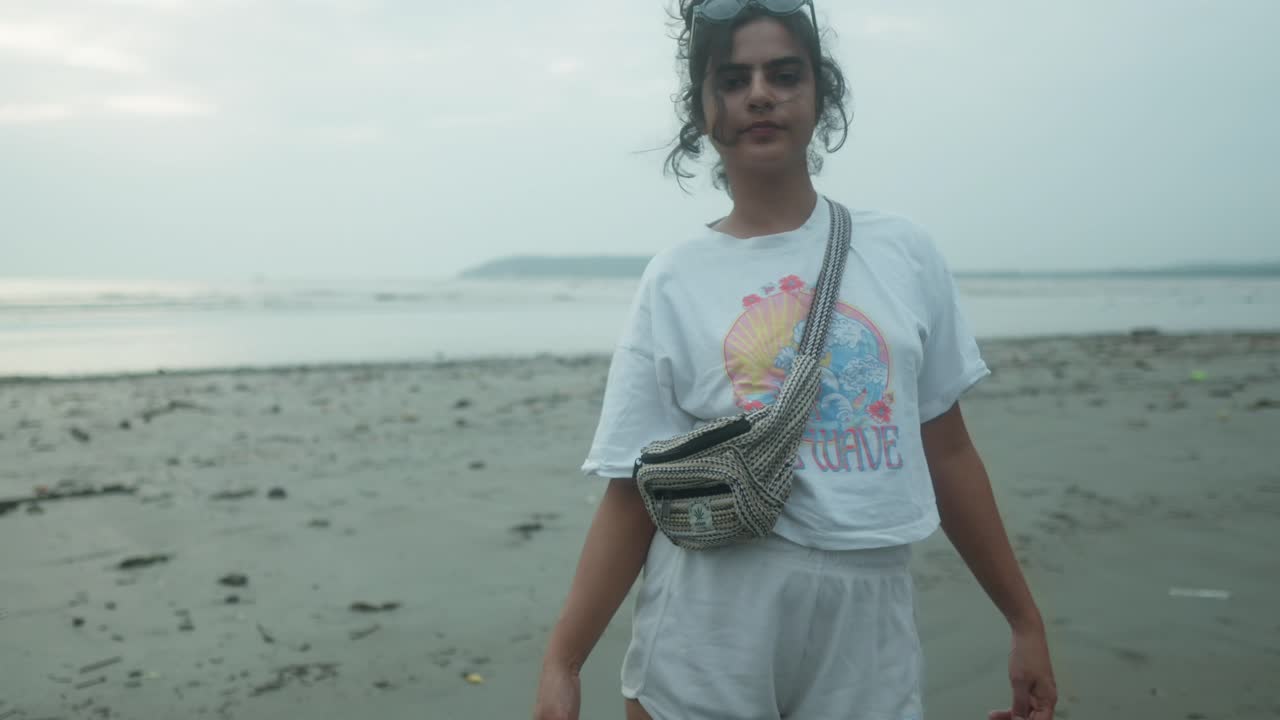 mujer joven relajada disfrutando de un paseo poniendo gafas de sol en la playa al atardecer