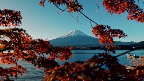 a breathtaking view of mount fuji reflected in the calm waters of lake kawaguchiko, surrounded by vivid red autumn foliage.