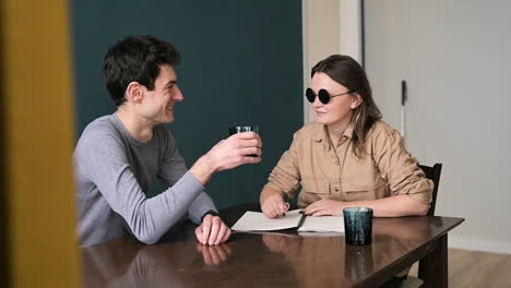 Man-And-Blind-Woman-In-Sunglasses-Sitting-At-Table-At-Home-Talking