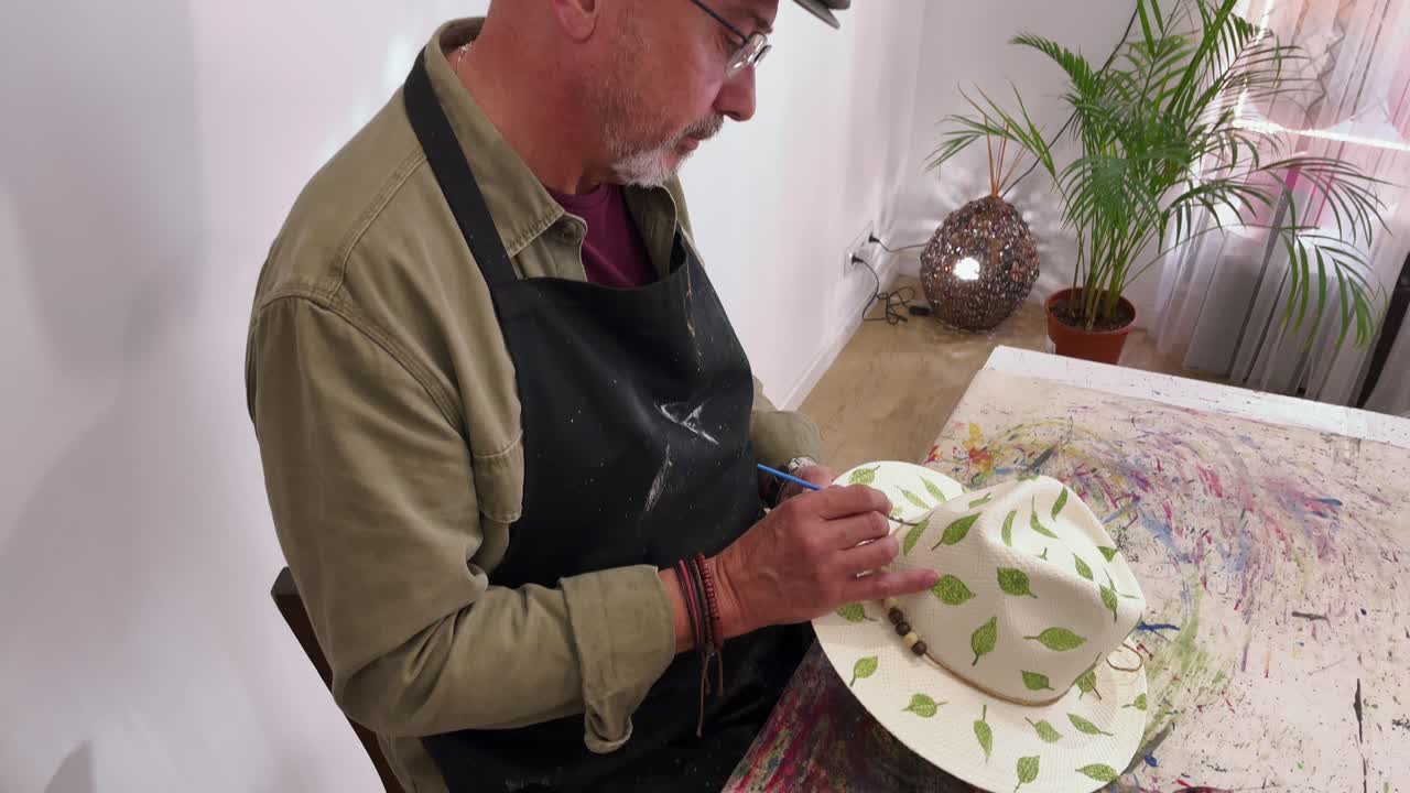 hombre maduro pintando en un sombrero de paja de moda en el taller